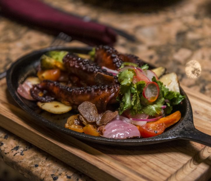 A gourmet seafood dish with octopus, vegetables, and seasonings served on a sizzling plate.