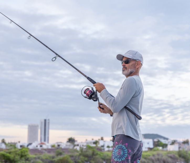 An older man fishing with a cityscape in the background.