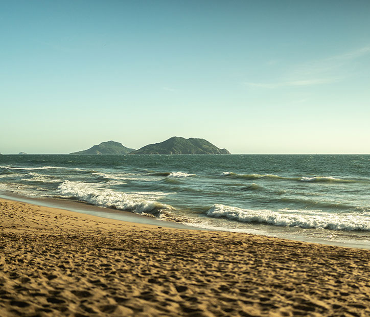 A scenic view of Mazatlán’s sandy beach with ocean waves and distant islands.