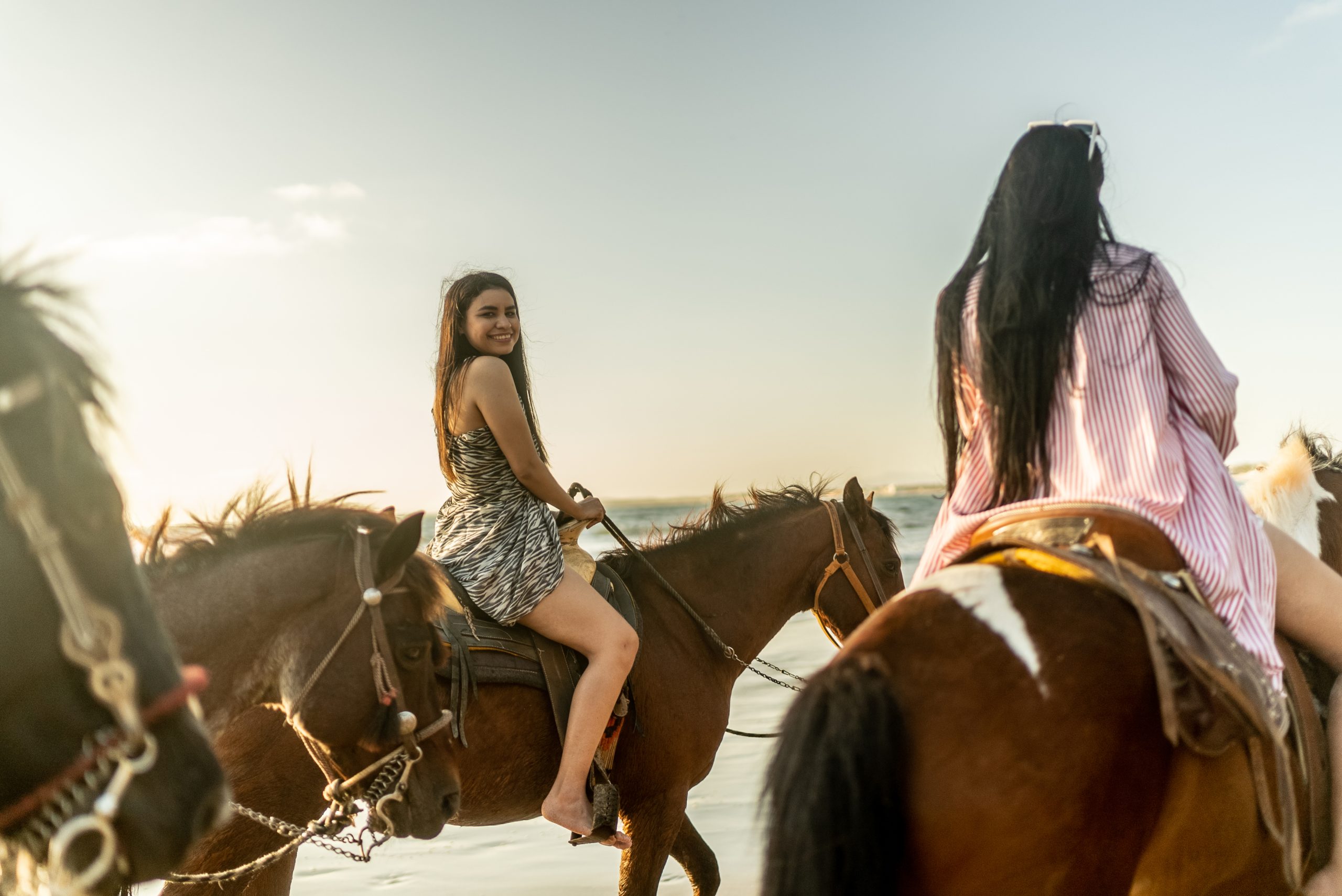 Two women riding horses along the beach at sunset.