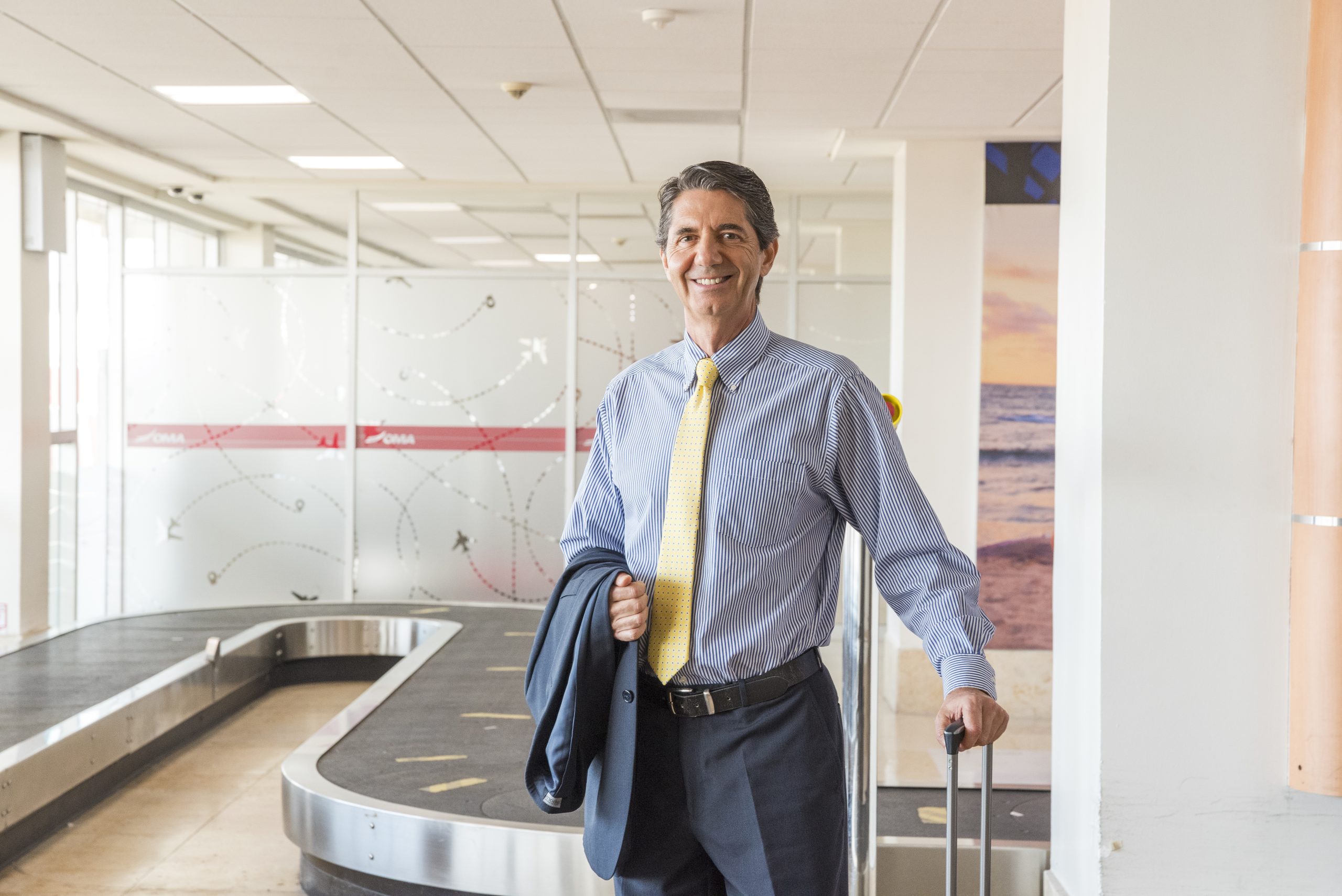 A businessman in a suit with a suitcase at the baggage claim in Mazatlán International Airport.