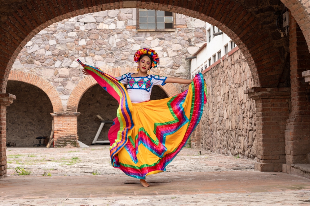 A woman in a colorful folkloric dress dancing in a historic courtyard.