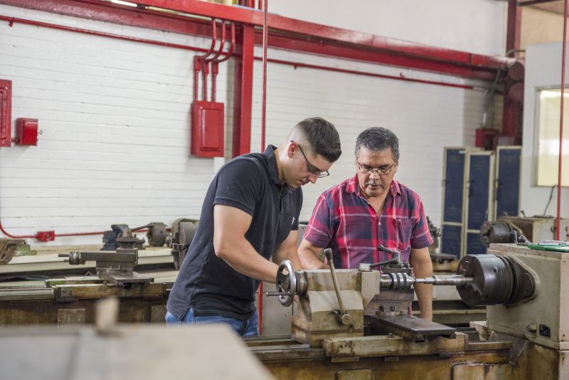 Tetakawi workforce development in Mazatlán, Mexico — skilled technician trains a young worker on industrial machinery in a hands-on learning environment